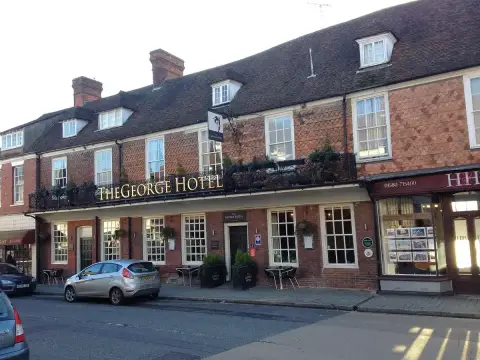 Long brick and tile-hung inn with dormer windows and iron balconies over the pavement