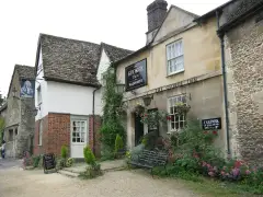 Stone and rendered inn with a black name board, lanterns and flowers along the front