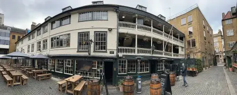 White inn with two tiers of open wooden galleries above a dark green bar front, in a cobbled yard