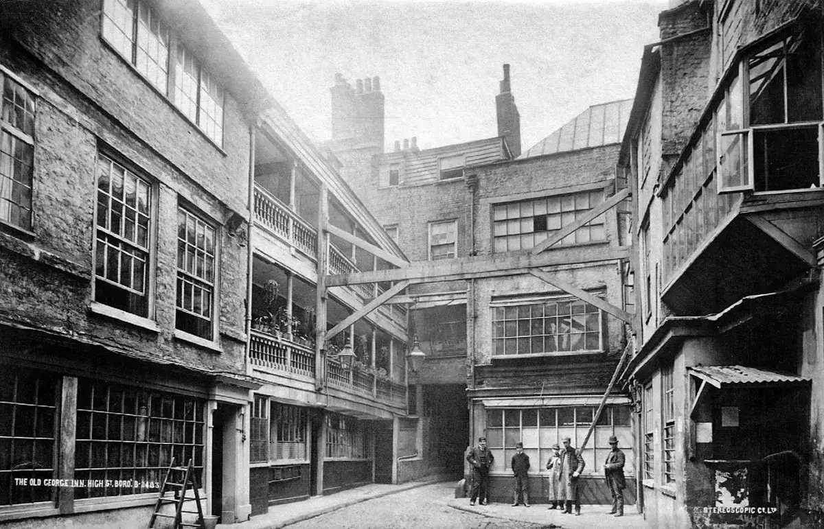 The galleried yard of the George in 1889, wooden galleries on the left and men standing by the range on the right