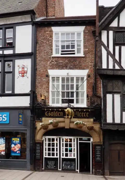 Narrow brick pub front with a gilded sheep over the door and a black lettered fascia