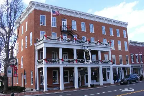 Four-storey red-brick hotel with a white two-tier porch and painted sign, on a main street