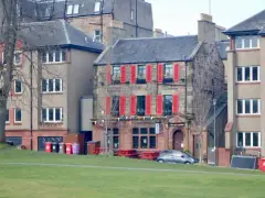 Stone tavern with bright red shutters and a lettered fascia, seen across the grass of the links