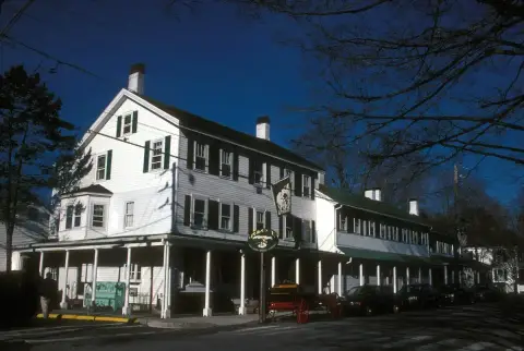 White clapboard inn of three storeys with green shutters, a colonnaded porch and hanging sign