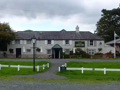 Long rendered inn with a slate roof, shuttered windows and a green name board, beside the road