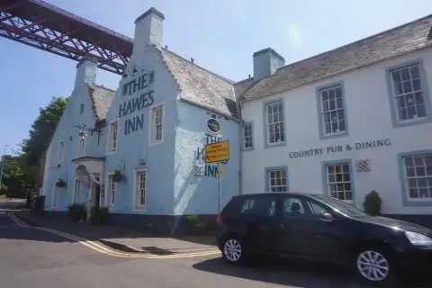 Pale blue crow-stepped inn with its name in large letters, the Forth Bridge girders overhead