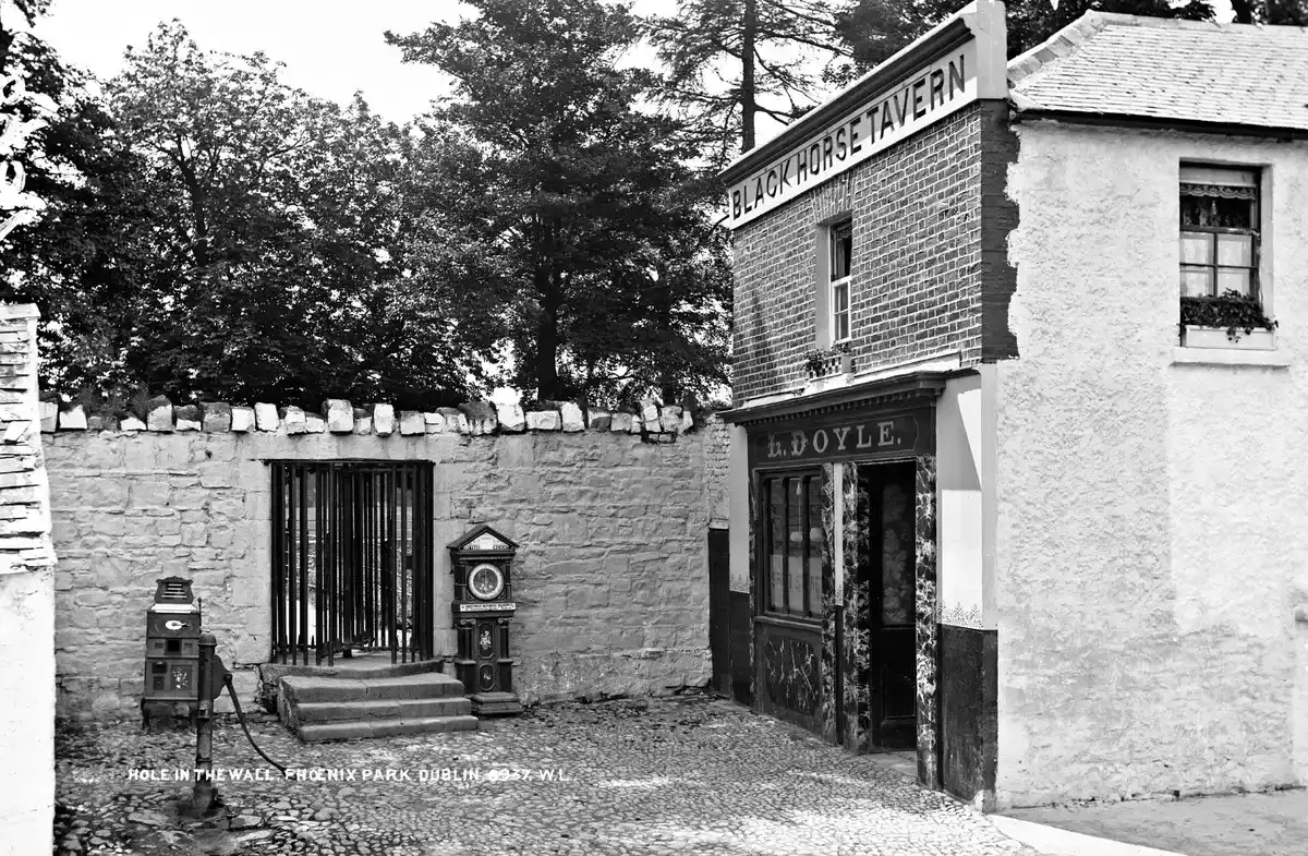 Black-and-white photograph of the Black Horse Tavern beside the Phoenix Park wall, with L. Doyle over the door and a gated opening in the wall