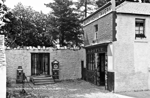 Black-and-white photograph of the Black Horse Tavern beside the Phoenix Park wall, with L. Doyle over the door and a gated opening in the wall