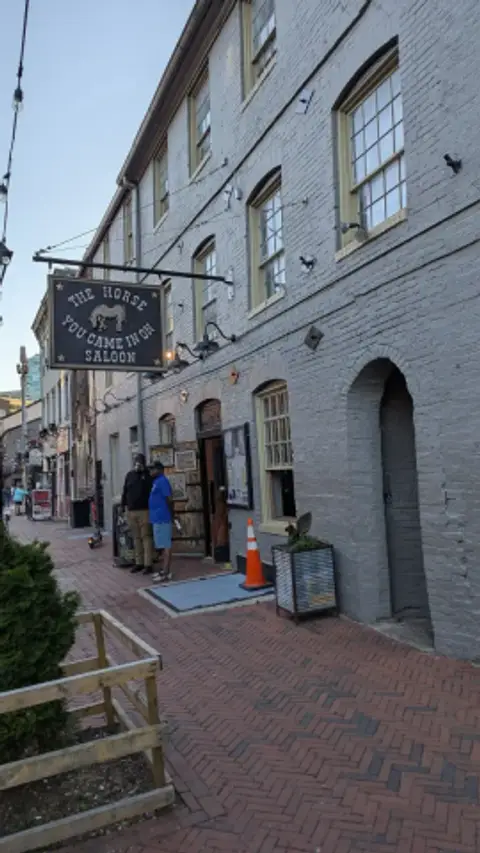 Grey-painted brick warehouse frontage with arched windows and a hanging saloon sign