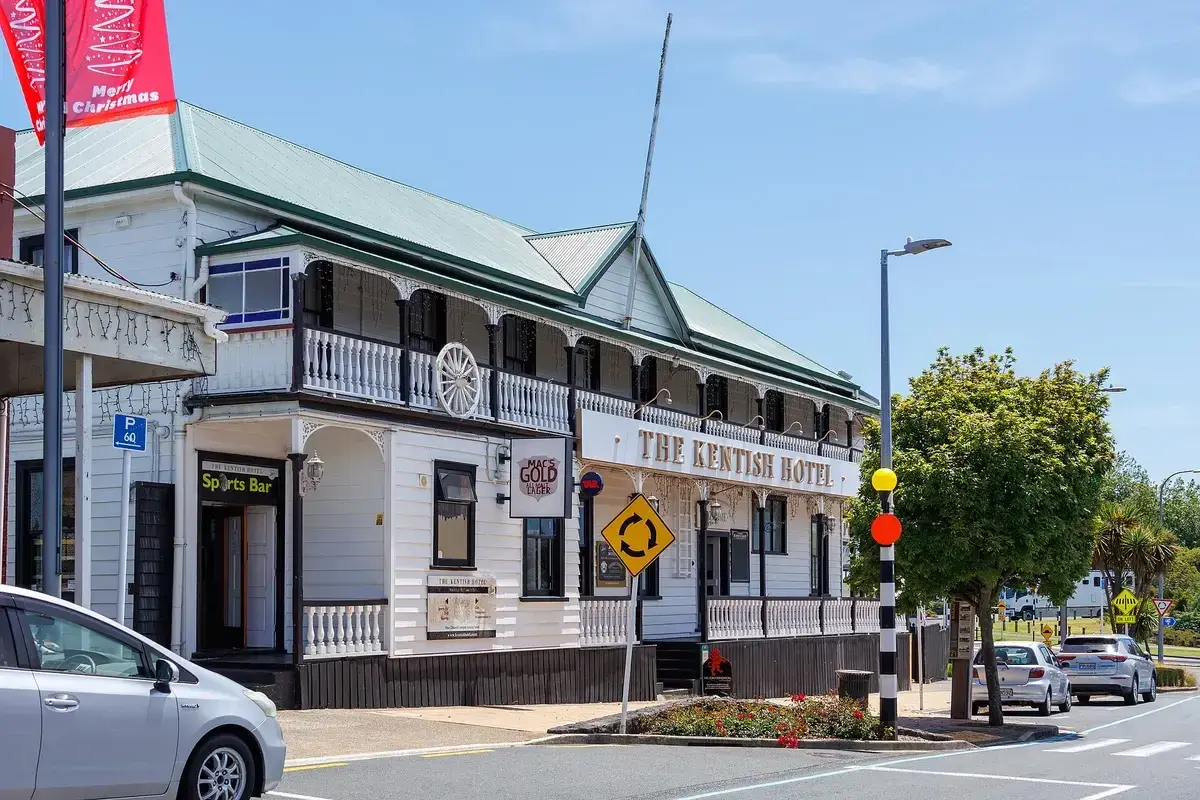 White weatherboard hotel with a green roof, lace-ironwork verandah and gold lettered sign
