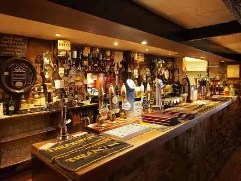 Long low bar counter under heavy beams, with handpumps, bottles and a stone rubble wall behind