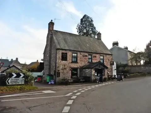 Old red sandstone inn with a steep slate roof, timber porch and painted name across the front