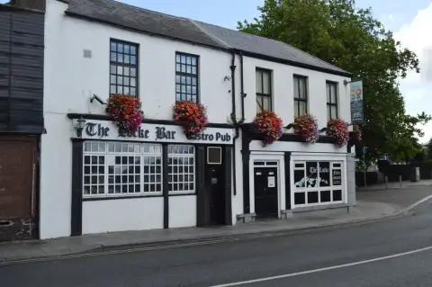 White pub with black timber trim, gold script lettering and rows of flower baskets