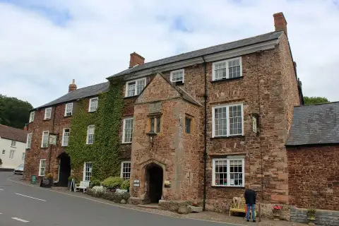 Long red sandstone inn with a two-storey gabled porch, sash windows and a carriage archway