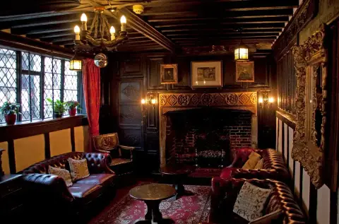 Panelled room with a carved stone fireplace, beamed ceiling, leaded windows and leather sofas
