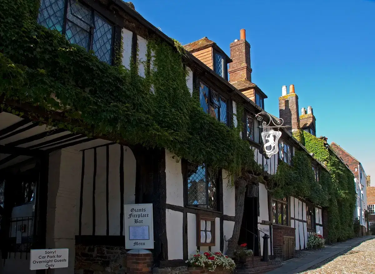 Timber-framed inn hung with ivy on a cobbled street, with leaded windows and a mermaid sign