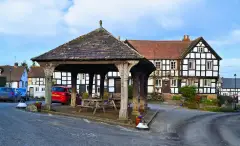 Timber-framed inn behind an open oak market hall on stone staddles, picnic tables under its roof