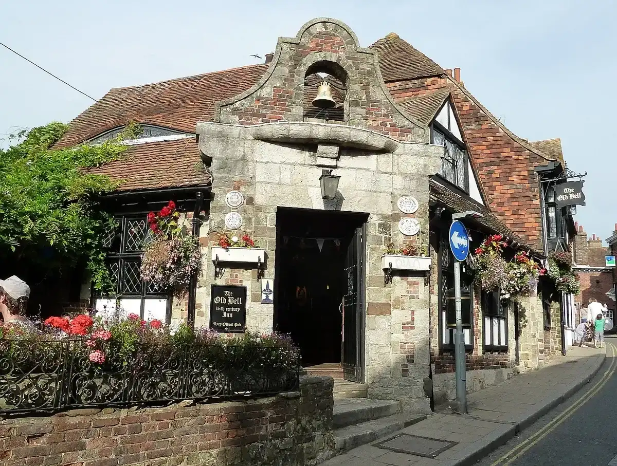 Stone porch topped by a bell in an arch, timber-framed inn behind with its name on the fascia