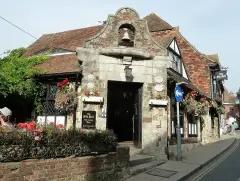 Stone porch topped by a bell in an arch, timber-framed inn behind with its name on the fascia