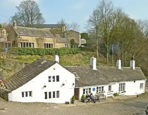 Long whitewashed inn with heavy stone-slate roof and white chimneys, in a wooded valley