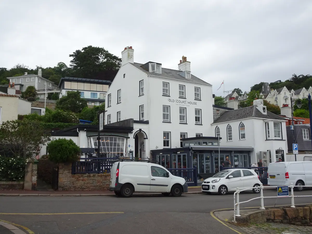 The white three-storey Old Court House Inn facing St Aubin's harbour, with its name on the front and a smaller Gothic-windowed wing