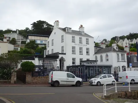 The white three-storey Old Court House Inn facing St Aubin's harbour, with its name on the front and a smaller Gothic-windowed wing