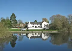 Long white thatched inn on the far bank of the Great Ouse, reflected in still water