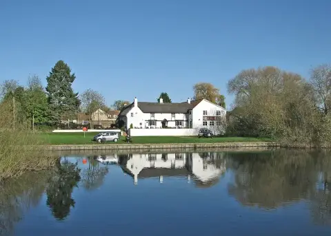 Long white thatched inn on the far bank of the Great Ouse, reflected in still water
