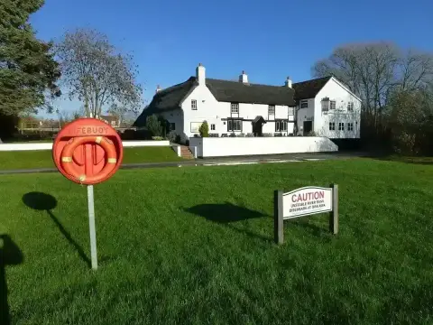 Whitewashed inn with a deep thatched roof, black timbers and white chimneys, seen across a lawn