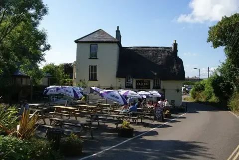 The Old Inn at Mullion from the road, thatched roof above picnic tables and parasols along the front