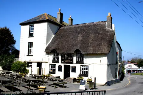 The thatched Old Inn at Mullion under a clear sky, its name board and St Austell Ales sign over the door