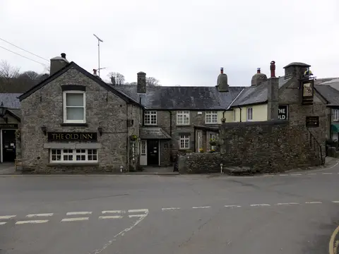 Granite front of The Old Inn at Widecombe, gold name board over the windows and the hanging sign at the right