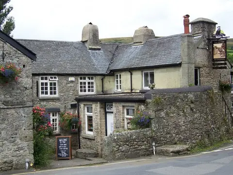The Old Inn’s long granite front in summer, hanging baskets by the door and the inn sign at the right