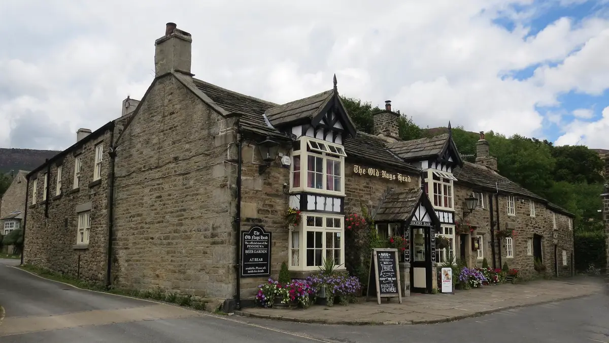 Gritstone pub with black-and-white gabled porches, its name in gold on the wall and moorland behind
