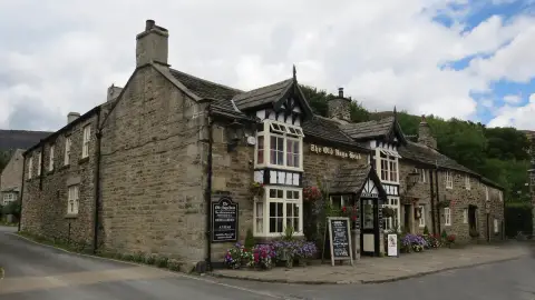 Gritstone pub with black-and-white gabled porches, its name in gold on the wall and moorland behind