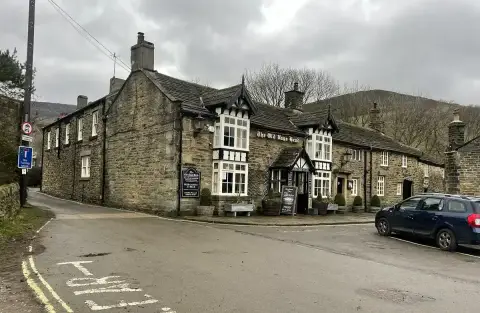 The pub on a grey winter day at a road junction, bare trees and the flank of Kinder behind