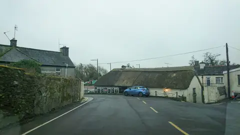 A long, low thatched pub at a bend in the village road at Killeagh, a car parked beside its wall