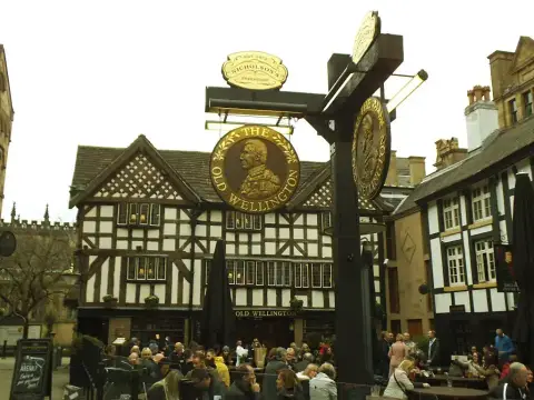 Black-and-white timber-framed pub with jettied floors behind a tall painted sign on a post