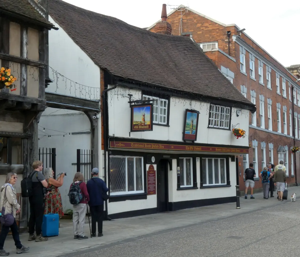 Timber-framed pub with a swept tiled roof, painted windmill sign, and visitors on the pavement outside