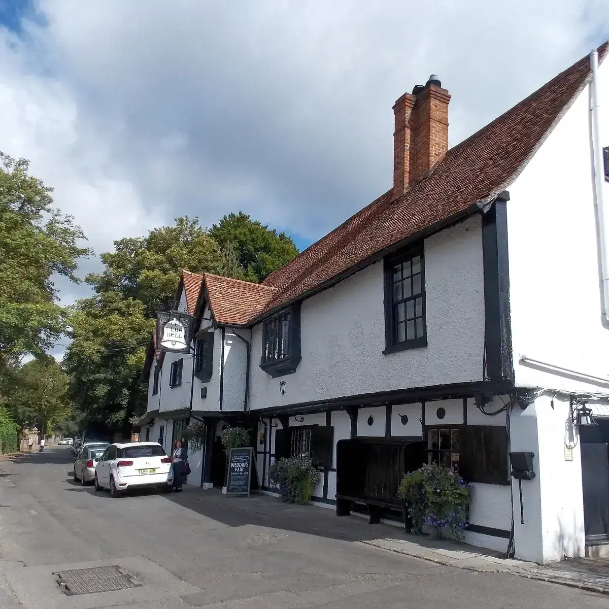 White rendered and timber-framed inn with a tiled roof, brick chimney and wrought-iron sign