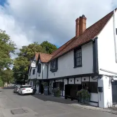 White rendered and timber-framed inn with a tiled roof, brick chimney and wrought-iron sign
