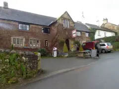 The granite front of the Oxenham Arms with its gabled porch and hanging inn sign