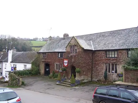 The Oxenham Arms along the village street, granite walls, slate roof and a swinging sign