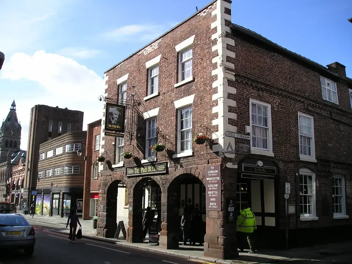 Three-storey brick inn on a street corner with a sandstone arcade, hanging sign and flower baskets