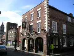 Three-storey brick inn on a street corner with a sandstone arcade, hanging sign and flower baskets
