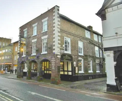 The same corner inn at dusk, its arcade lit and a mileage board listing London and Bath