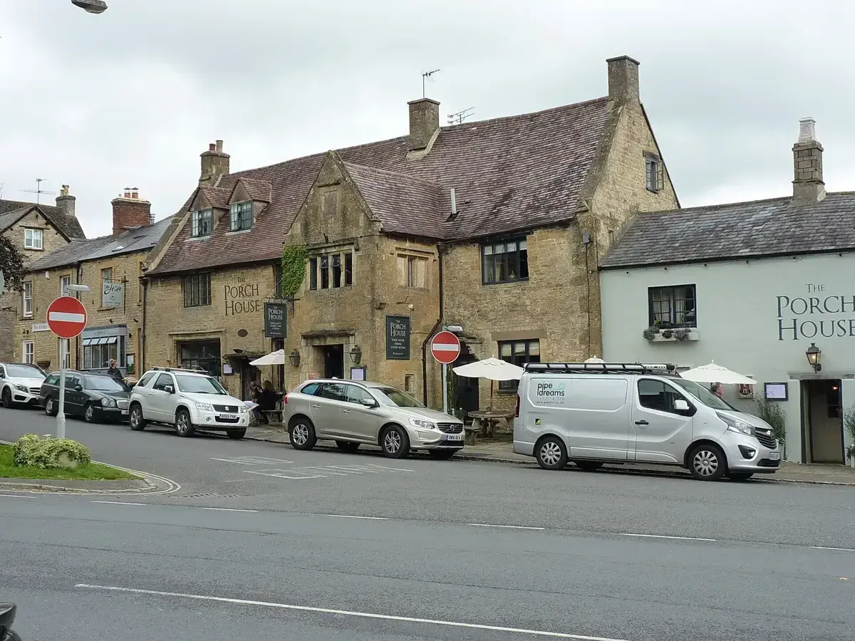 Cotswold limestone frontage with mullioned windows and a stone porch, under a steep tiled roof