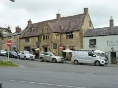 Cotswold limestone frontage with mullioned windows and a stone porch, under a steep tiled roof