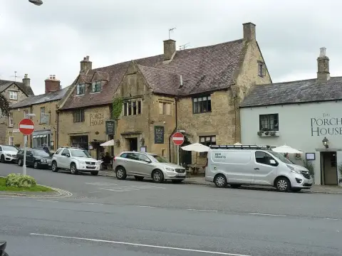 Cotswold limestone frontage with mullioned windows and a stone porch, under a steep tiled roof