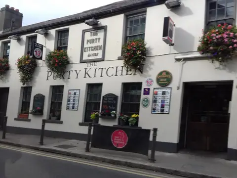 White pub front on Old Dunleary Road lettered The Purty Kitchen, with hanging flower baskets and a framed sign